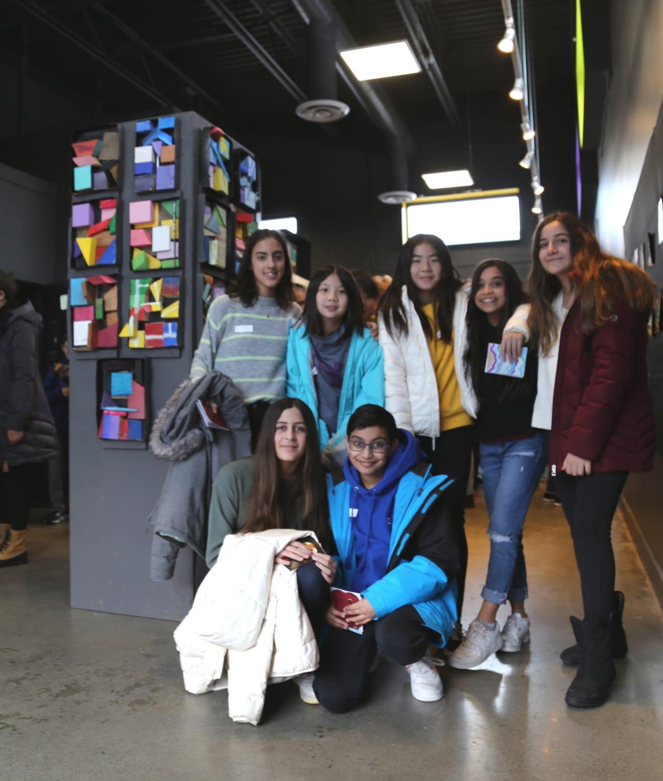 Grade 7 students pose beside their Kurt Schwitters inspired collaborative art pieces from the Reach to Teach: Immersed in the Arts Program.